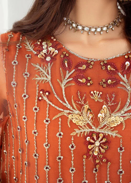 Close-up of an orange embroidered garment with intricate designs and jewelry.