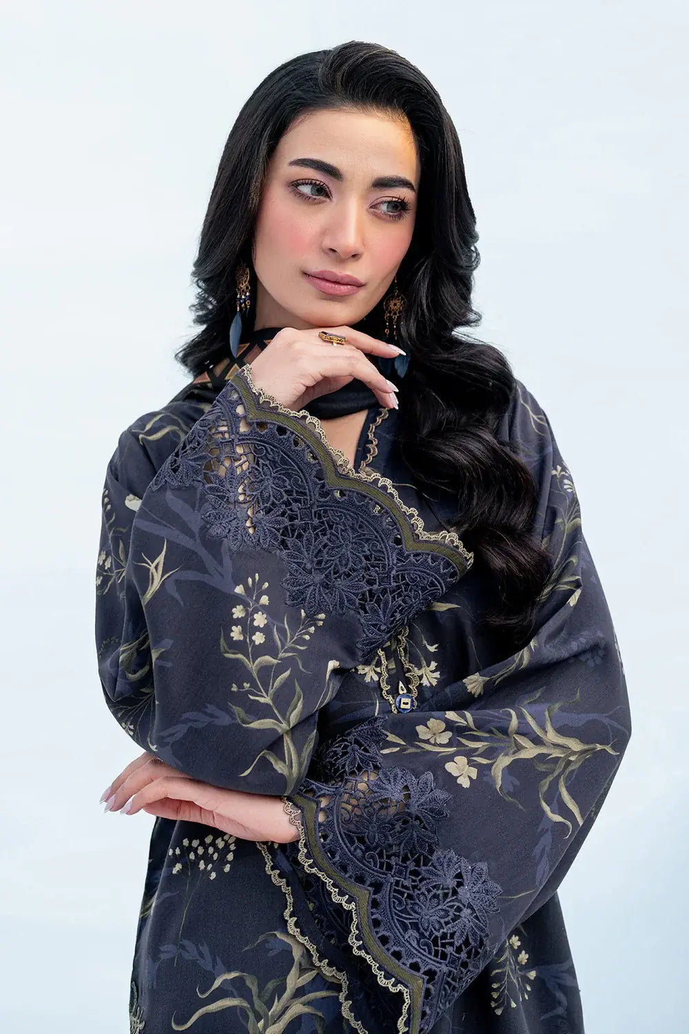 Woman wearing a dark blue embroidered traditional outfit against a light gray background