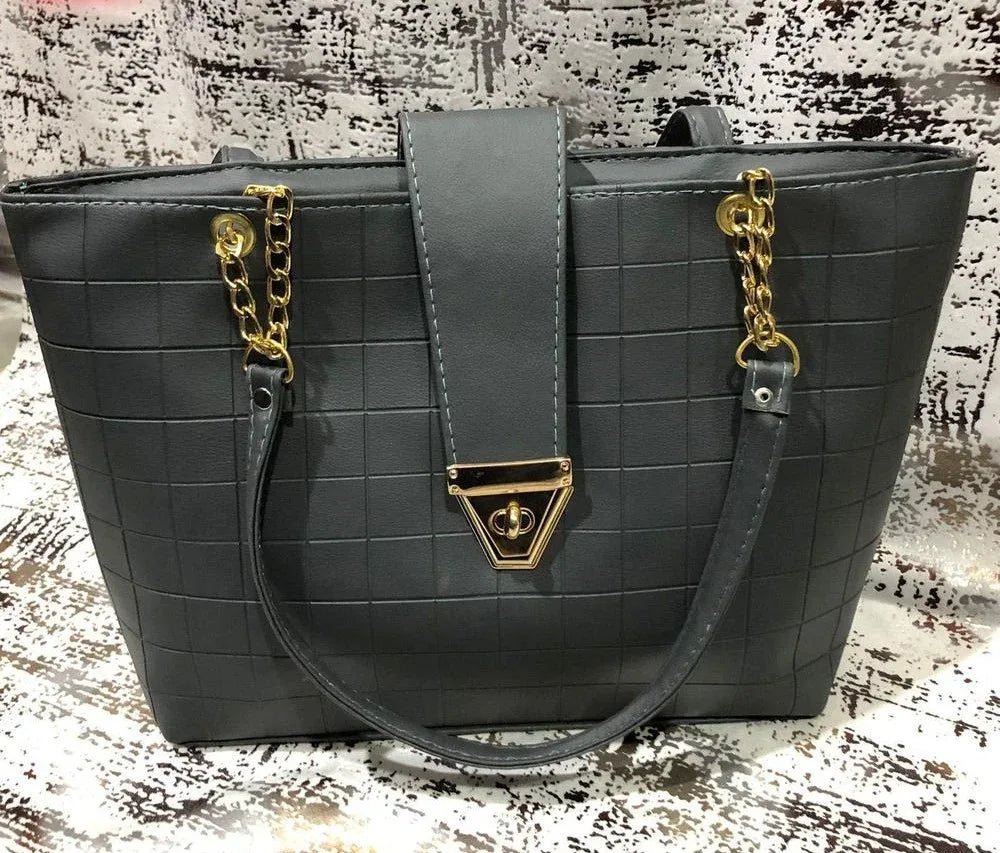 Gray quilted handbag with gold chain details on a textured surface