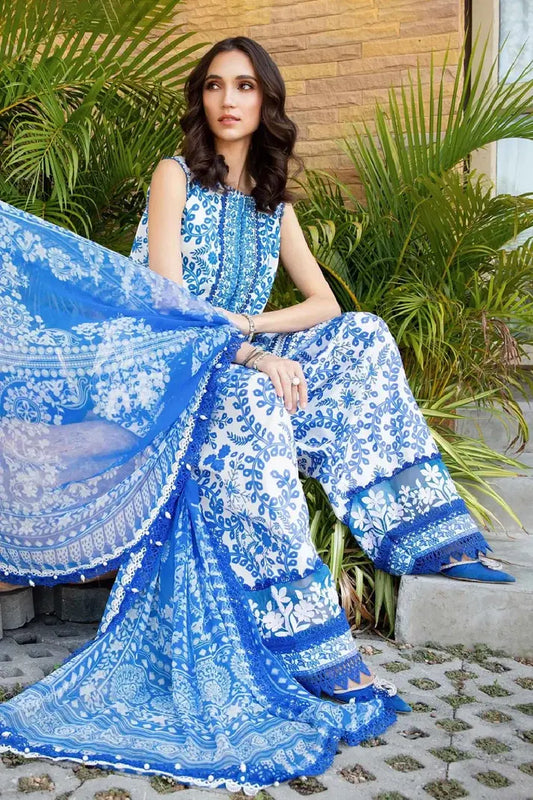 Woman in a blue and white embroidered saree sitting outdoors with plants in the background