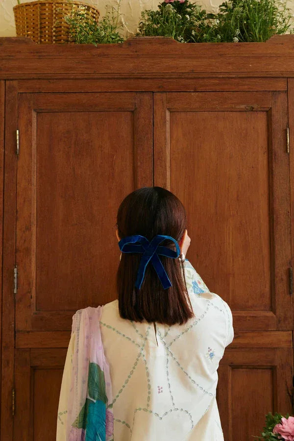 Person with a blue ribbon in their hair standing in front of a wooden cabinet.