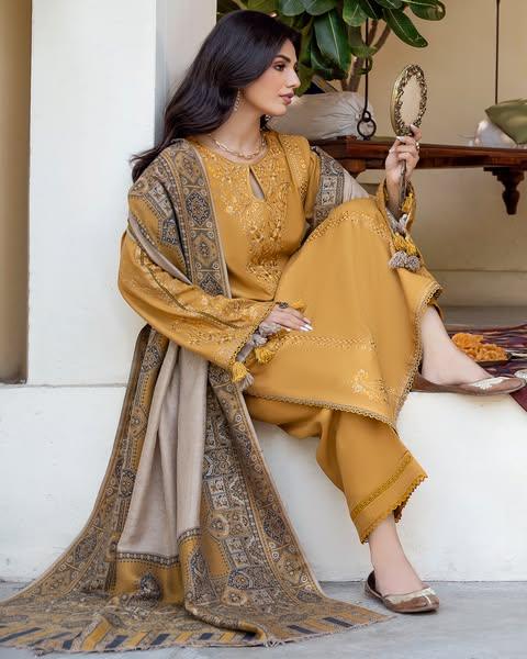 Woman in a mustard yellow traditional outfit with intricate patterns, sitting on steps.