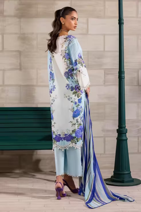 Woman in a floral dress with a long scarf standing against a textured wall.