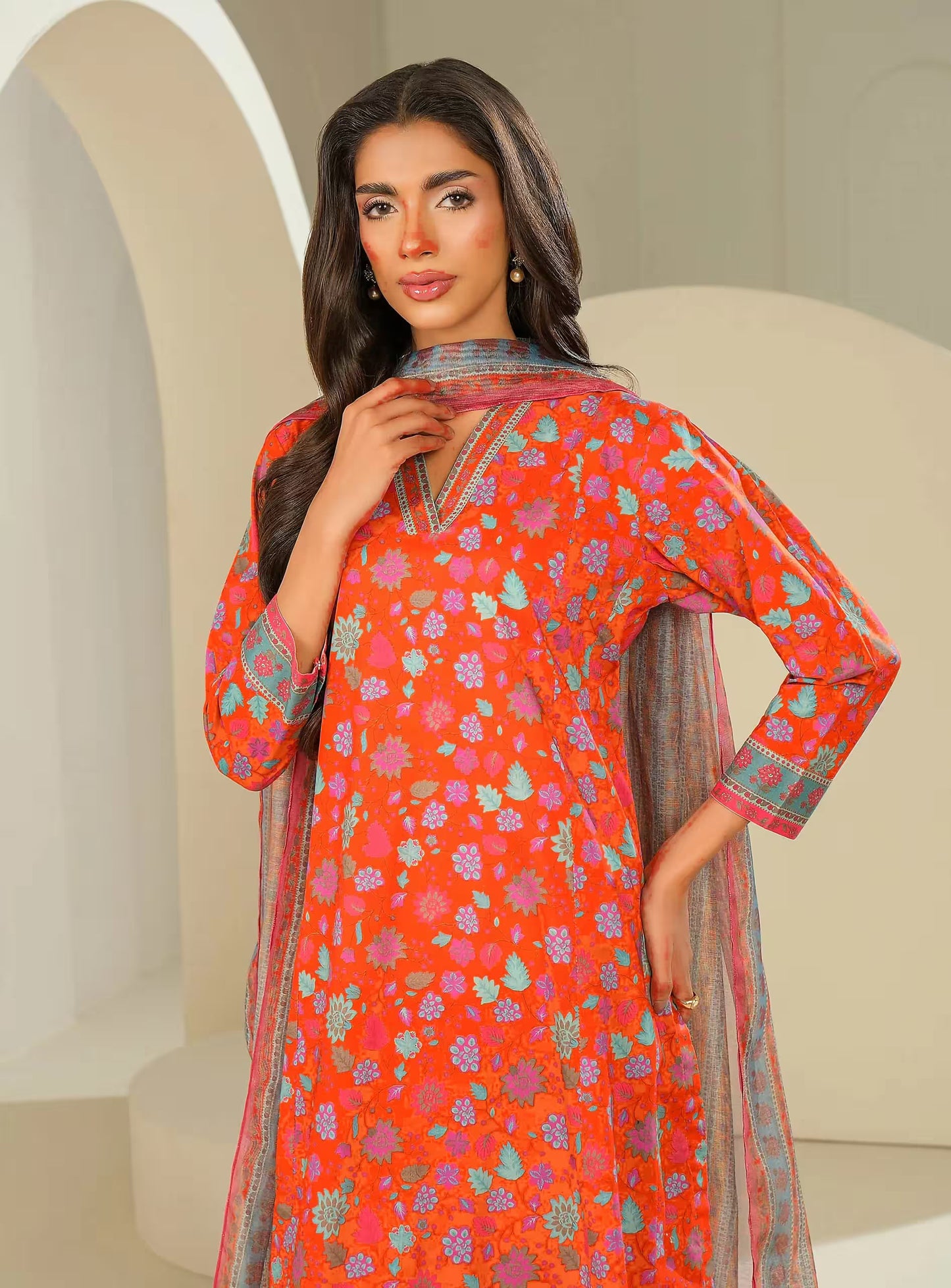 Woman wearing a vibrant orange traditional outfit with floral patterns in a neutral setting