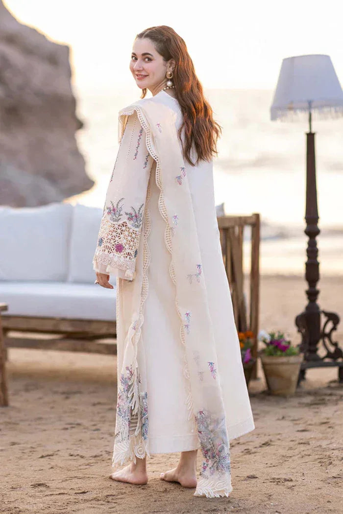 Woman in a white embroidered outfit standing on a sandy beach with a blurred background