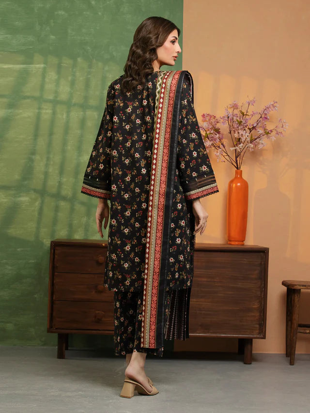 Woman wearing a black floral dress with a red border in a room with a wooden cabinet and vase.