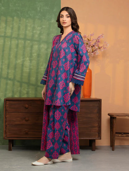Woman wearing a blue and pink traditional outfit standing in a room with a wooden dresser and vase.
