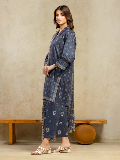 Woman wearing a blue patterned outfit standing against a beige wall.