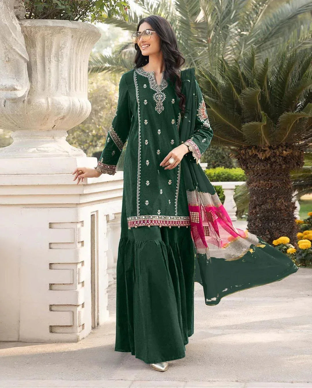 Woman in a green traditional outfit with embroidery standing outdoors.