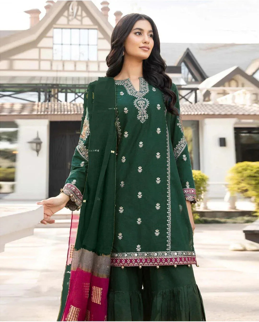 Woman in a green embroidered outfit standing in front of a building.