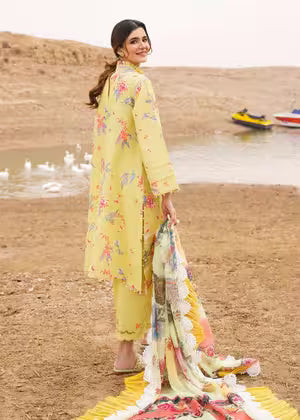 Woman in a yellow floral outfit standing by a lake with boats in the background