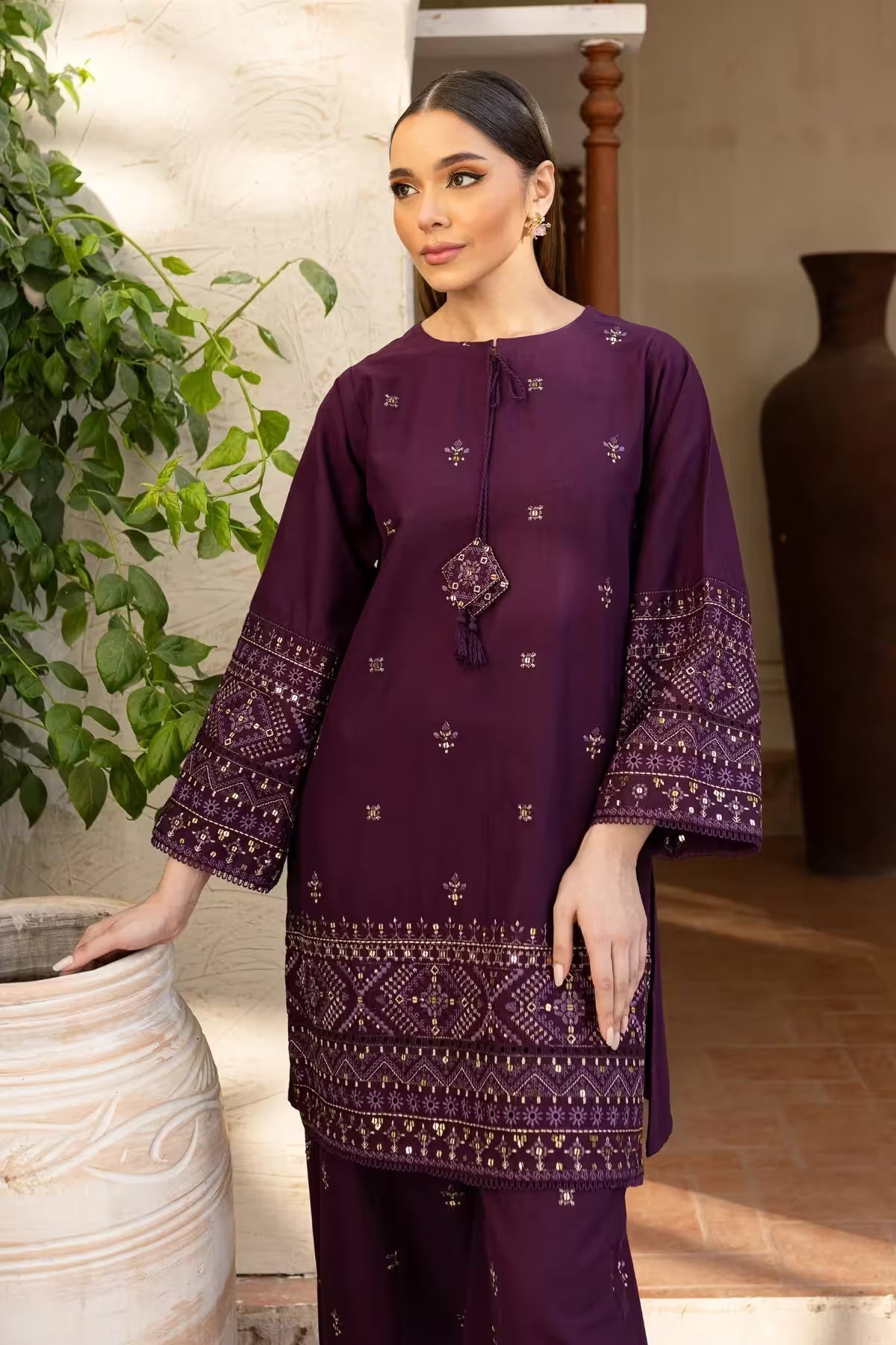Woman wearing a purple embroidered outfit standing indoors with decorative elements.