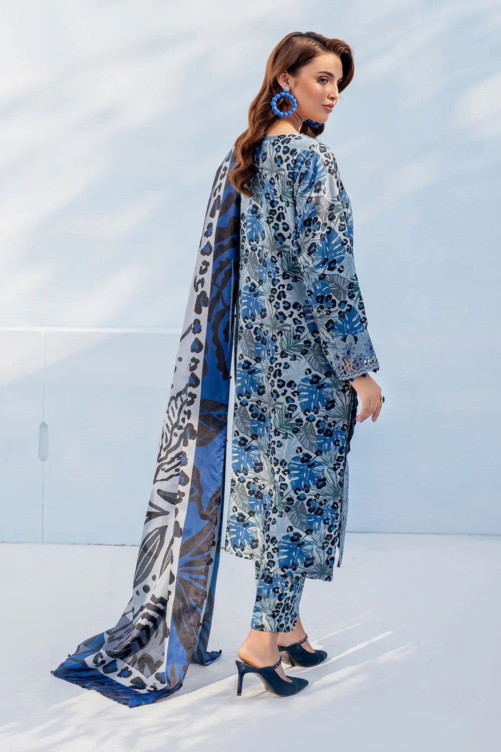Woman wearing a blue floral outfit with a long scarf against a white background