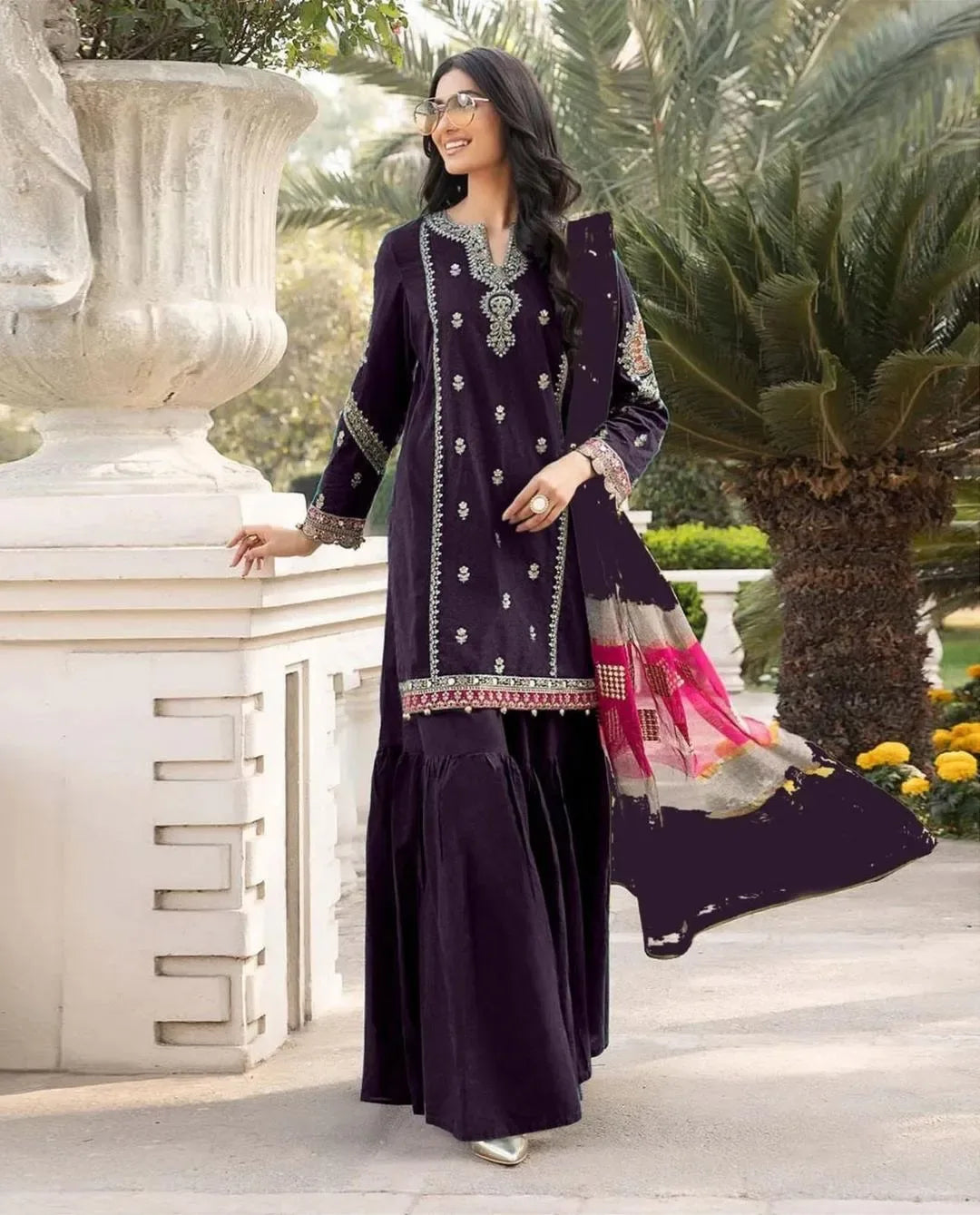 Woman in a dark purple traditional outfit with intricate embroidery standing outdoors.