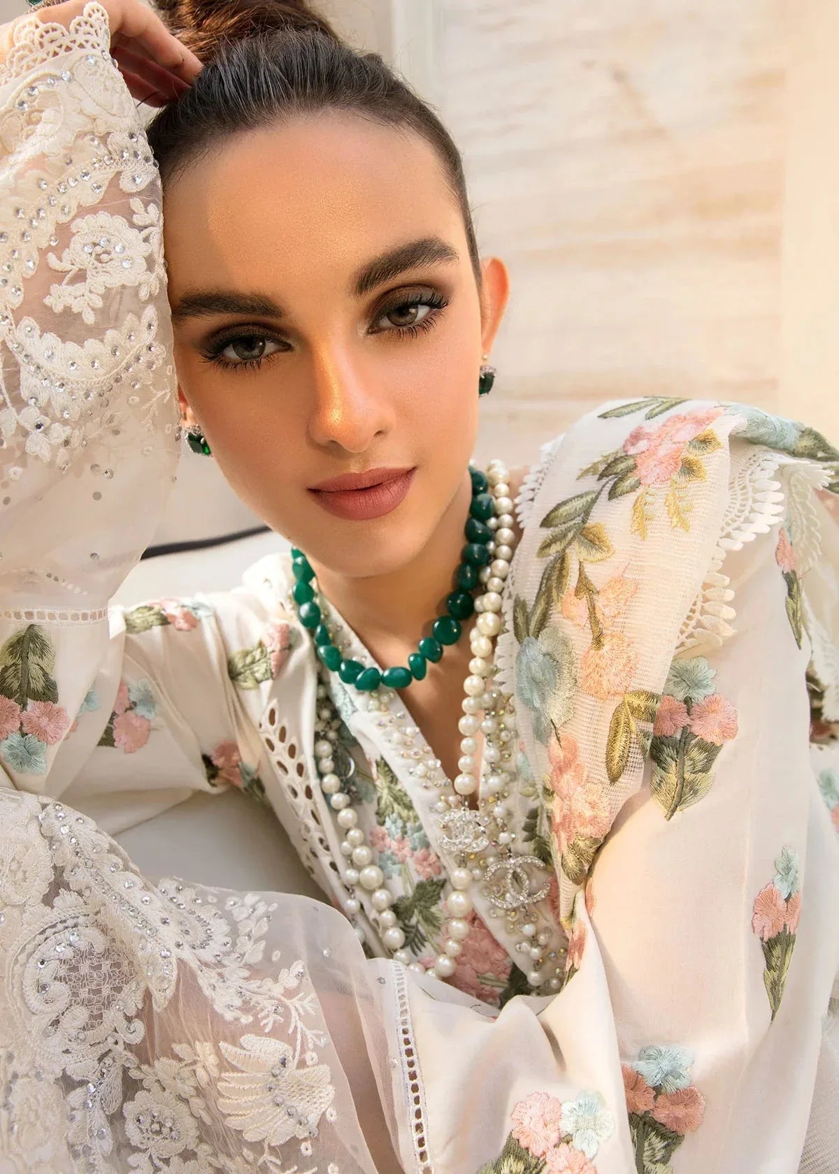 Woman wearing a floral embroidered outfit with a green necklace and pearl necklace.