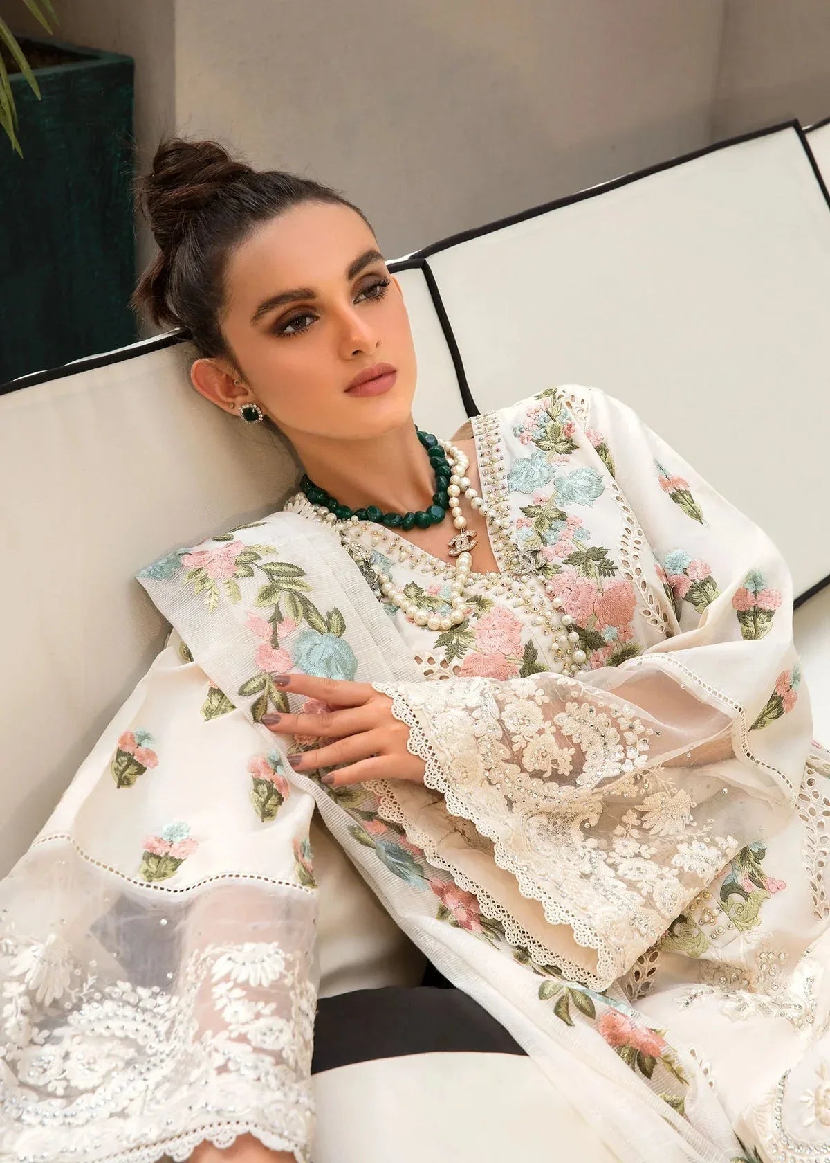 Woman wearing a white embroidered traditional outfit with floral patterns, sitting on a couch.