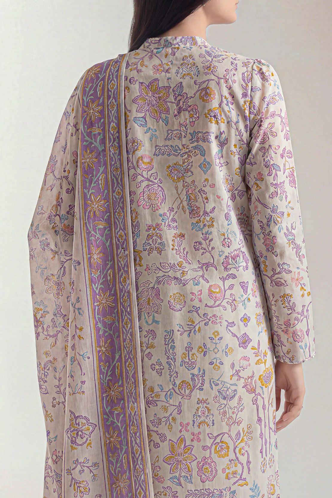 Woman wearing a floral patterned outfit with a sheer dupatta on a plain background