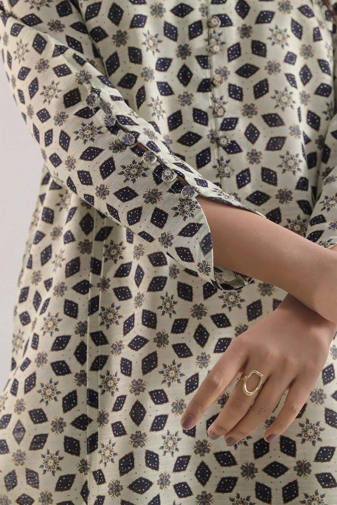 Close-up of a person wearing a patterned dress with a gold ring on a white background