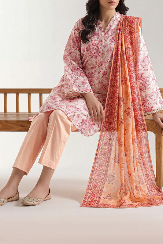 Woman sitting on a bench wearing a pink and white floral outfit with an orange and red patterned dupatta.