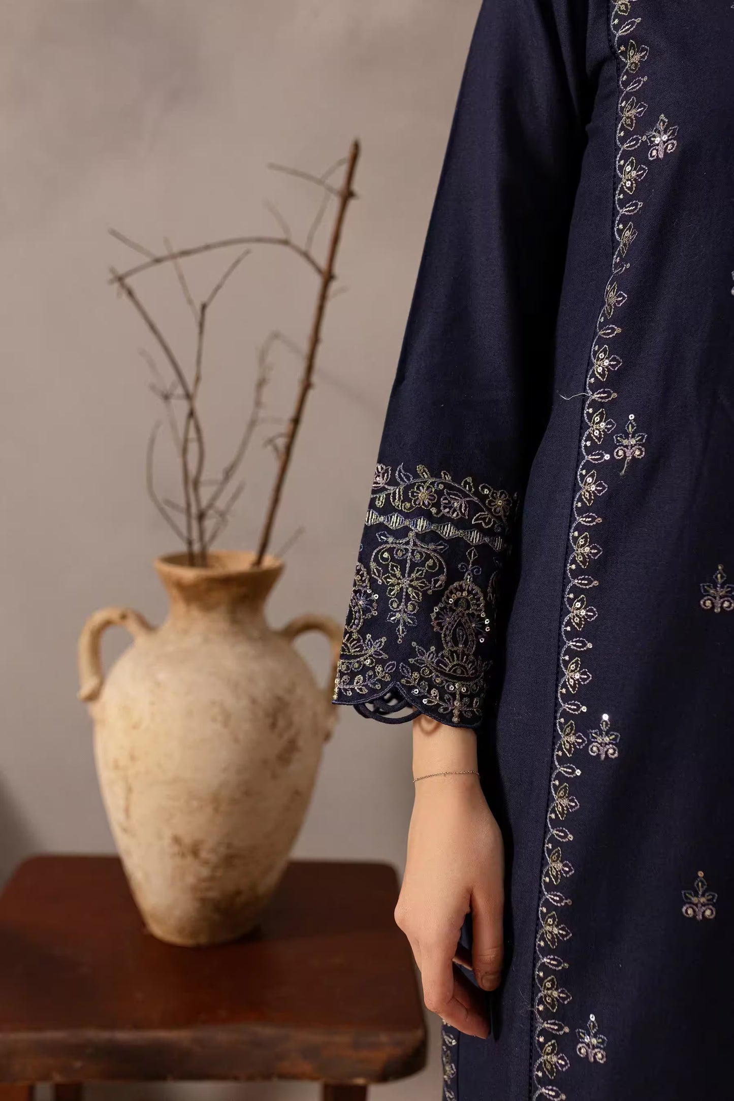 Navy blue embroidered garment with a rustic vase and branches in the background