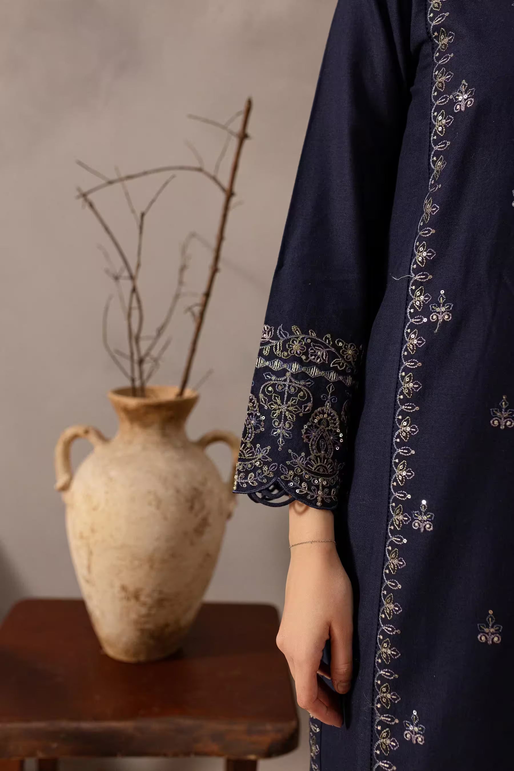 Navy blue embroidered garment with a rustic vase and branches in the background