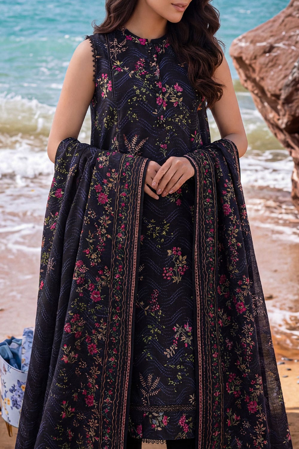 Woman in a dark floral dress standing on a beach with ocean in the background
