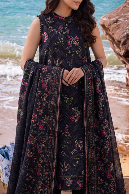 Woman in a dark floral dress standing on a beach with ocean in the background