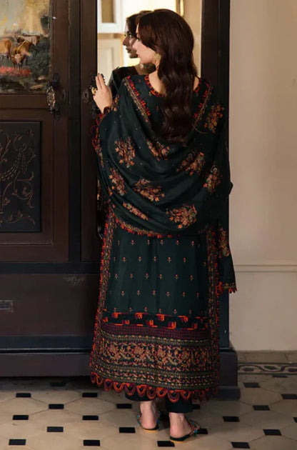 Woman wearing a dark green traditional outfit with intricate patterns in a room.