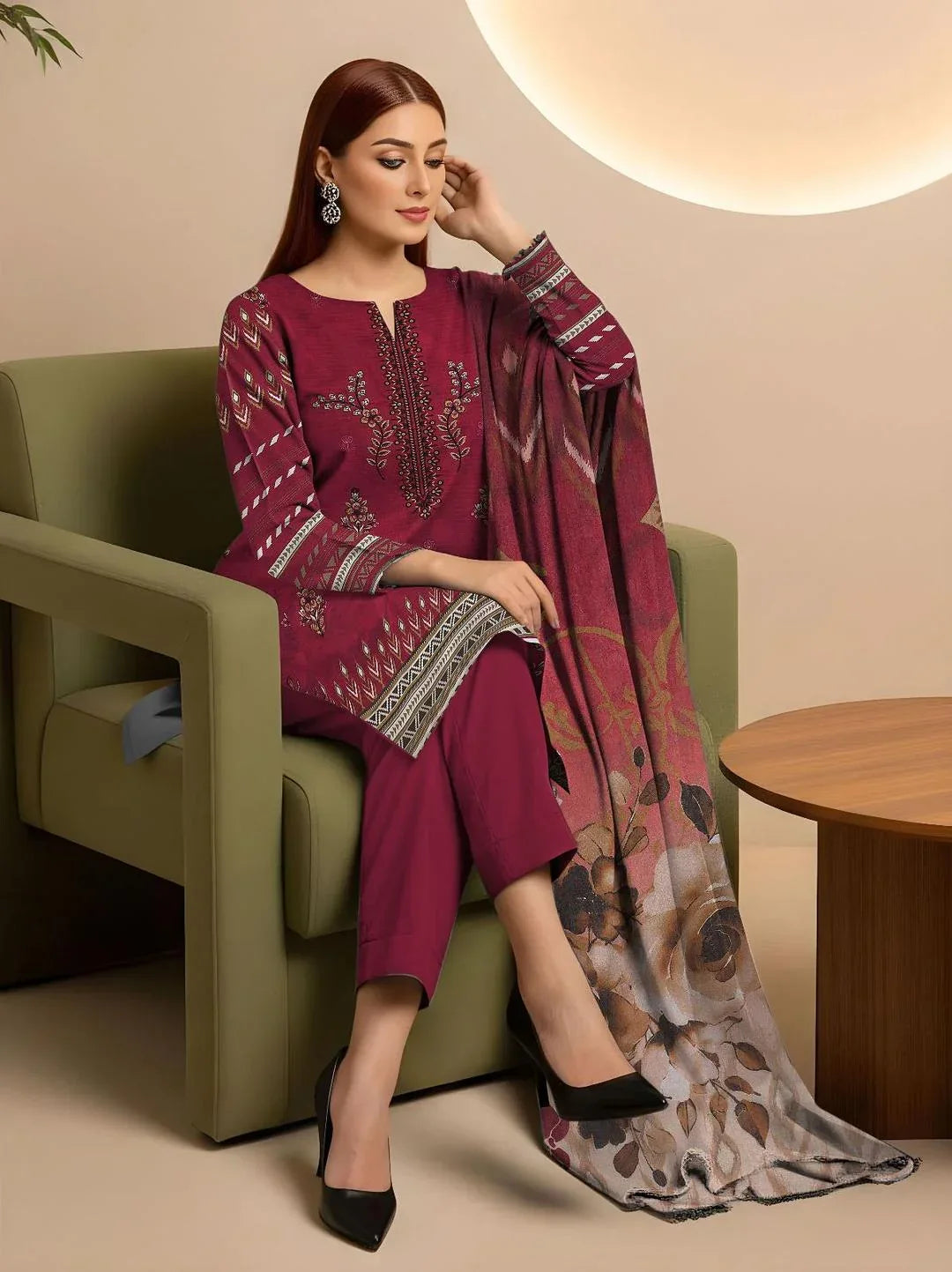 Woman in a maroon embroidered outfit sitting on a green chair with a patterned scarf.