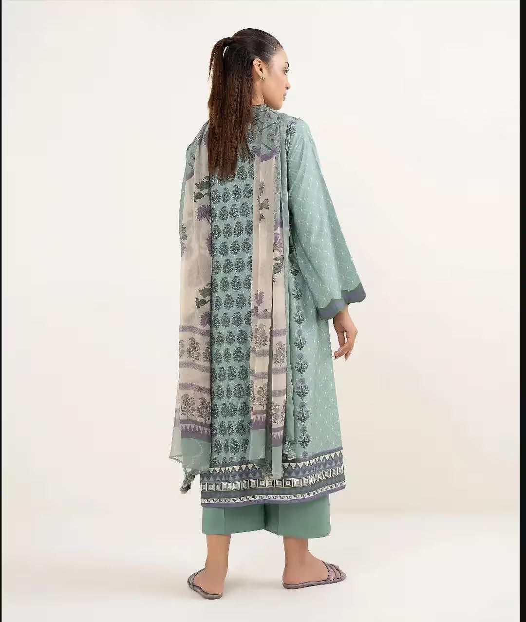 Woman wearing a green traditional outfit with a patterned dupatta on a white background
