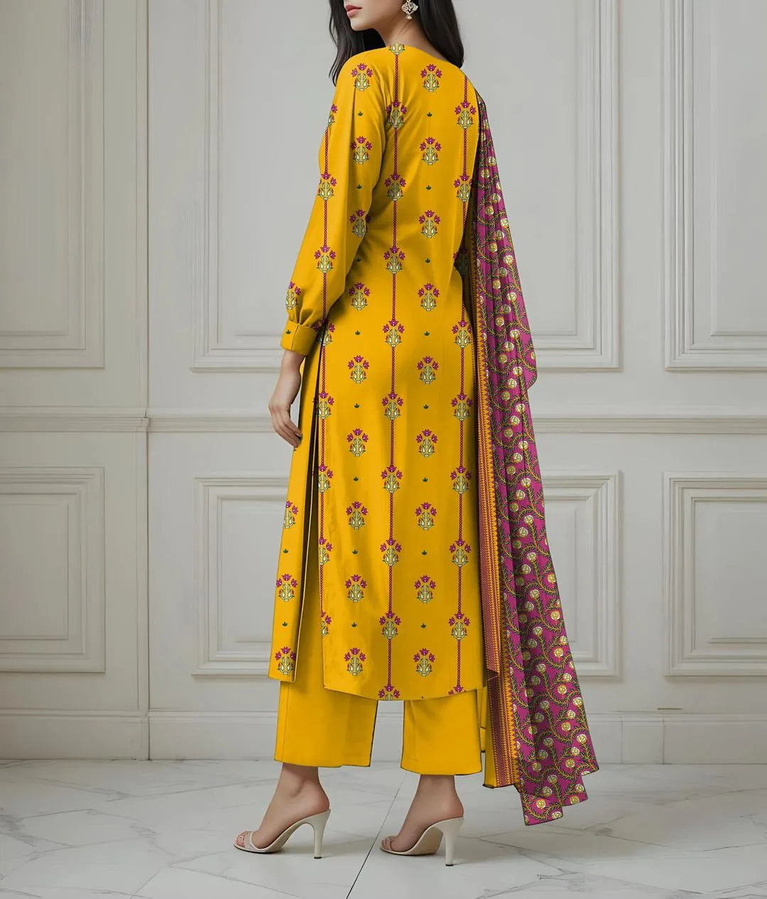 Woman wearing a yellow floral outfit with a pink dupatta against a white paneled wall.