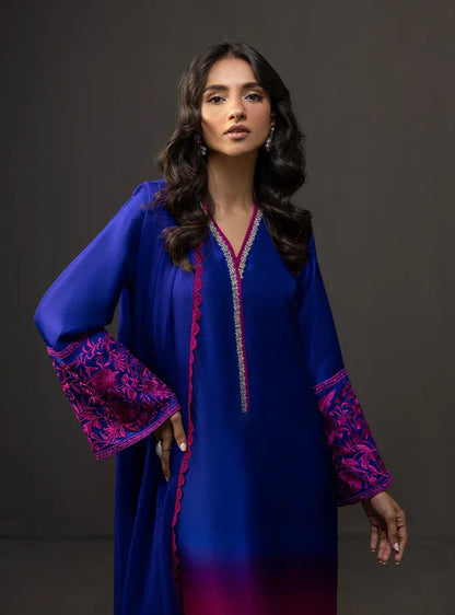 Woman wearing a blue dress with pink embroidery against a dark background