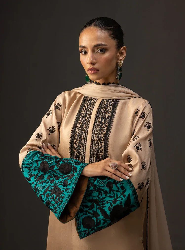 Woman wearing a beige and teal embroidered outfit against a dark background