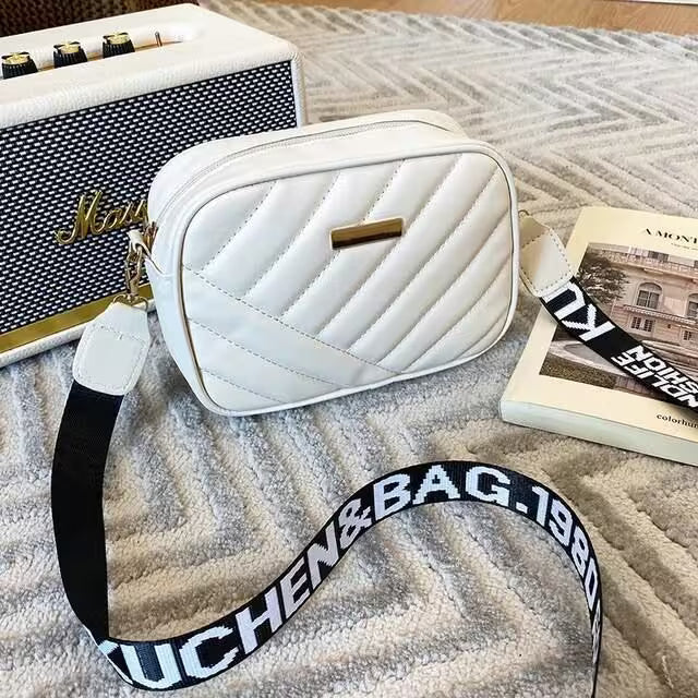 White quilted handbag with a black strap on a textured surface next to a Marshall amplifier and book.