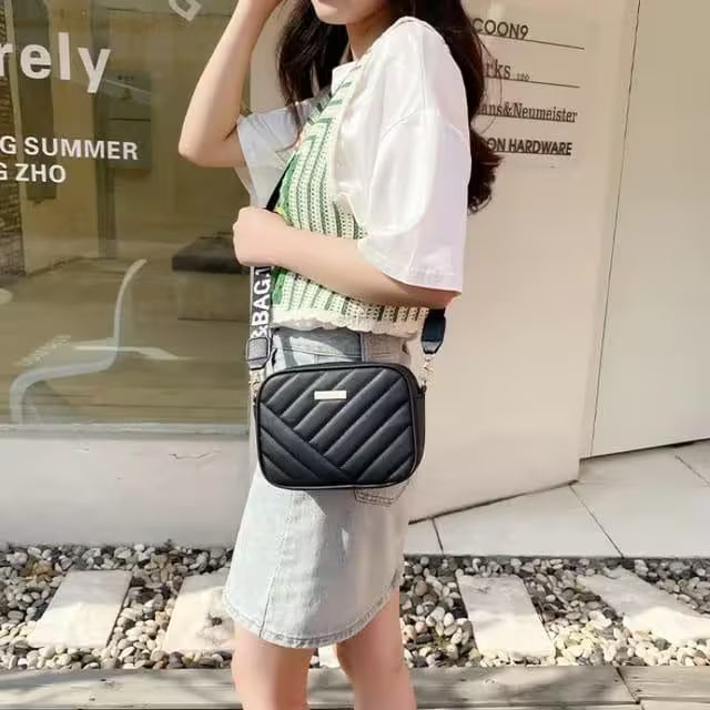 Person holding a black quilted handbag in front of a store window