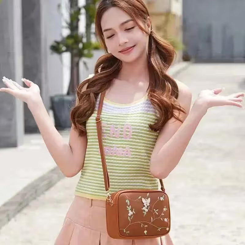 Woman holding a brown crossbody bag with floral design outdoors