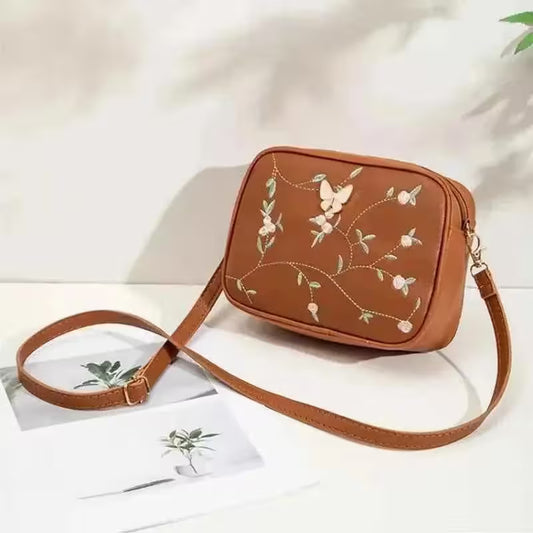 Brown crossbody bag with floral embroidery on a white background