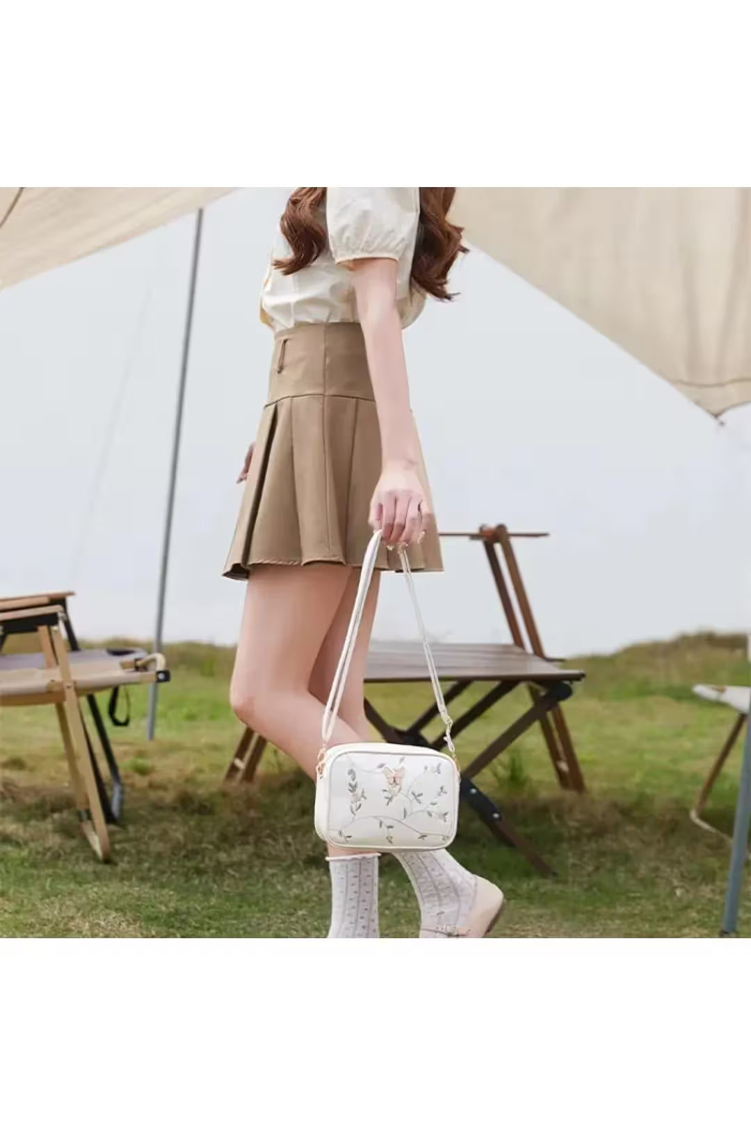 Woman holding a white handbag with floral design in an outdoor setting