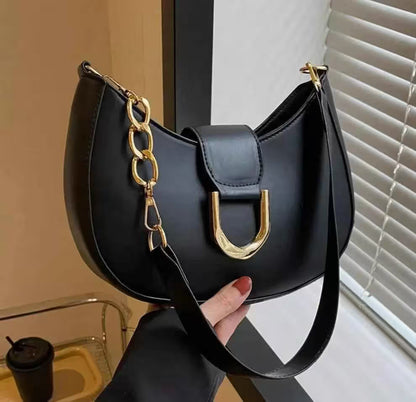 Black handbag with gold chain detail held by a hand, against a neutral background.