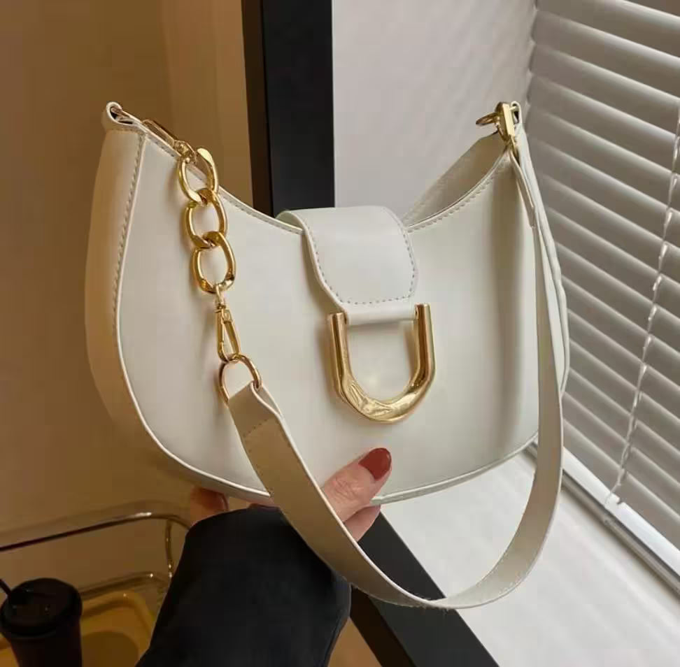 White handbag with gold chain and handle held by a person indoors.