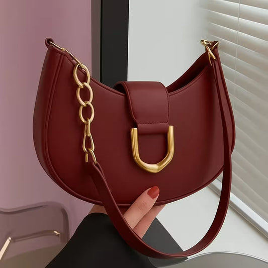 Red handbag with gold chain detail held by a hand against a neutral background