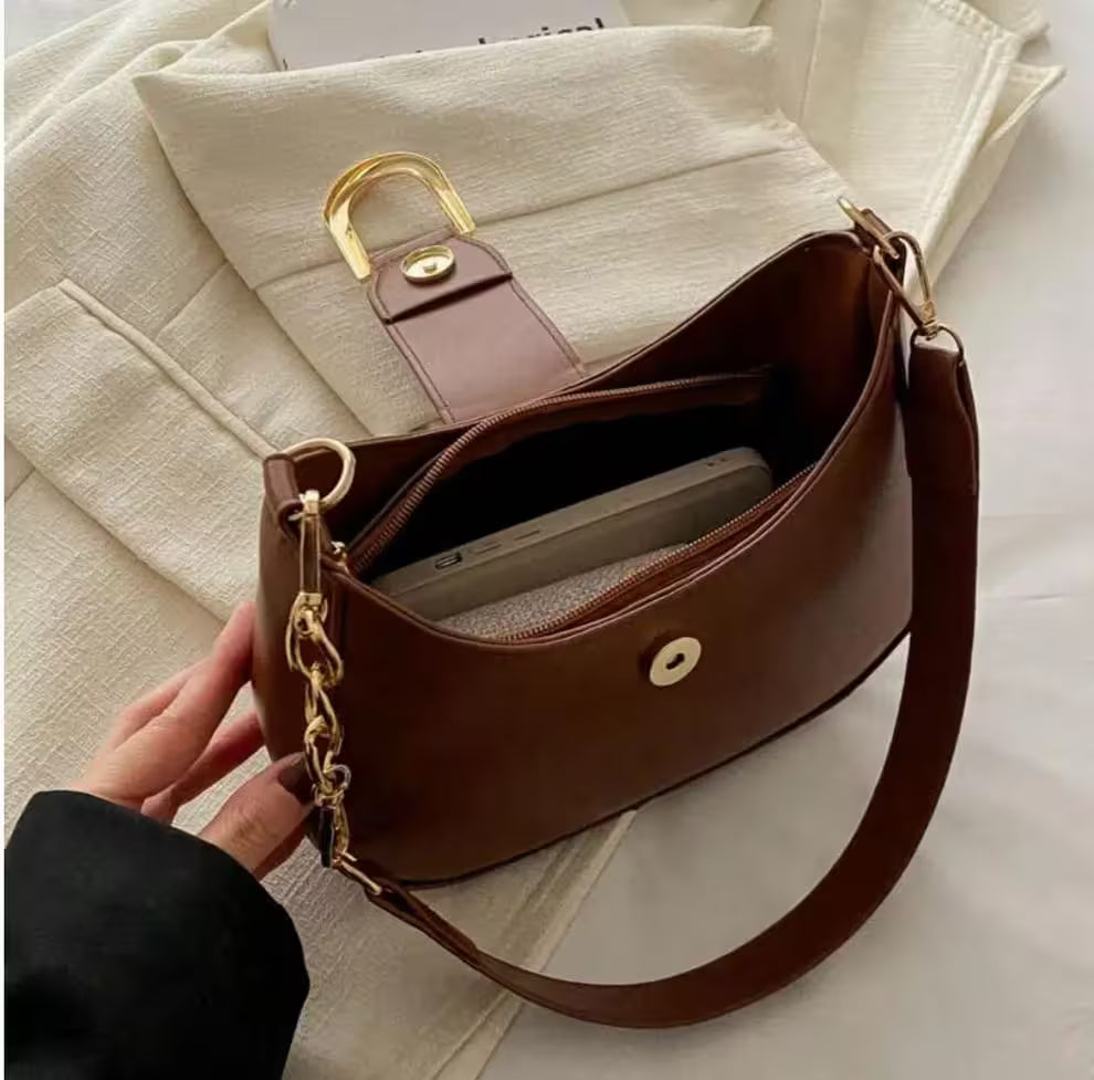 Brown handbag with gold accents held by a hand on a light background