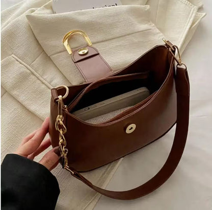 Brown handbag with gold accents held by a hand on a light background
