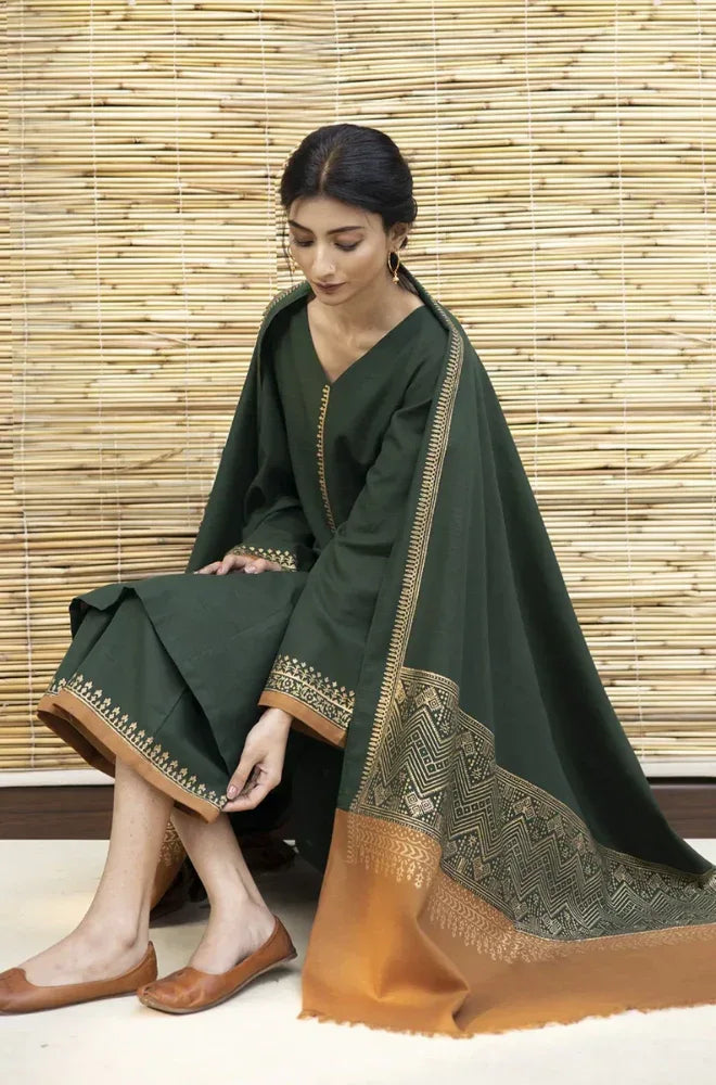 Woman wearing a dark green traditional outfit with gold embroidery against a wooden panel background