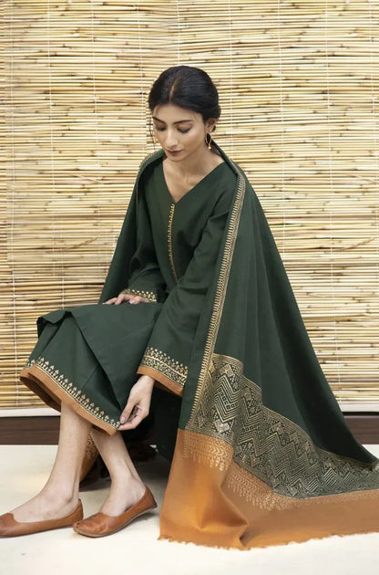 Woman wearing a dark green traditional outfit with gold embroidery against a wooden panel background