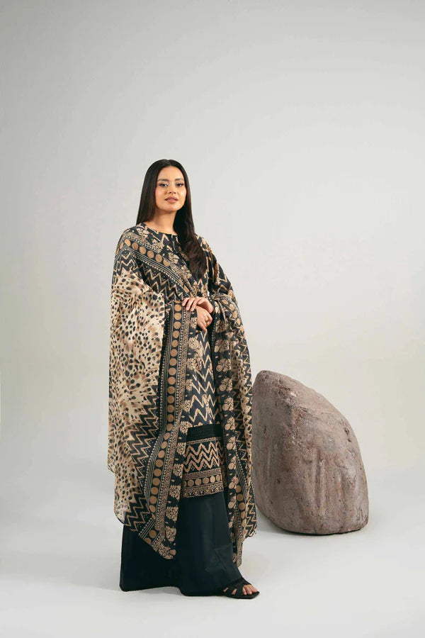 Woman wearing a long, patterned coat over a black outfit, standing next to a textured gray ottoman on a white background.
