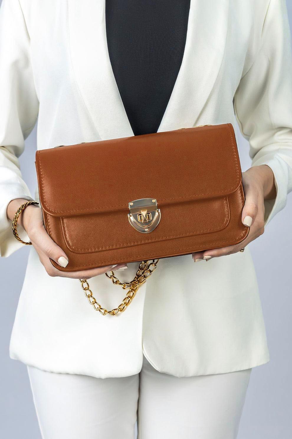 Person holding a brown handbag with a gold chain on a light gray background
