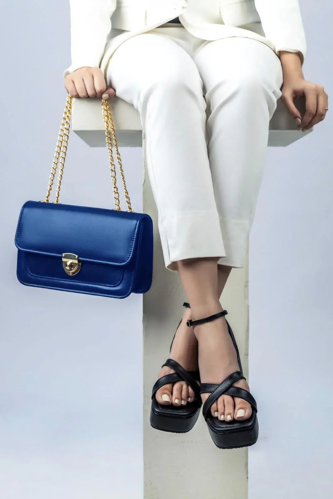 Person wearing white pants and black sandals with a blue handbag on a light gray background