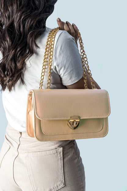 Beige handbag with gold chain strap worn by a person against a light blue background