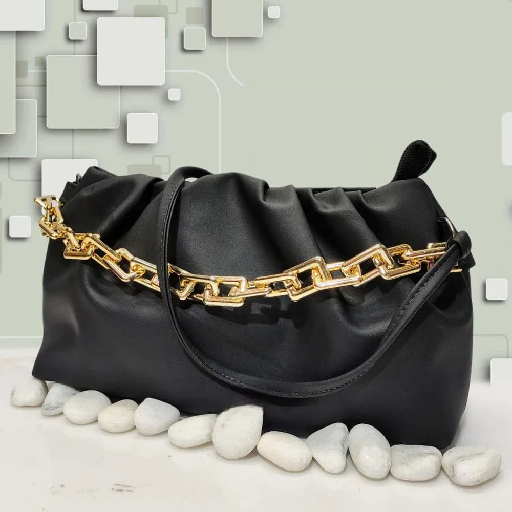Black handbag with gold chain detail on a light gray background
